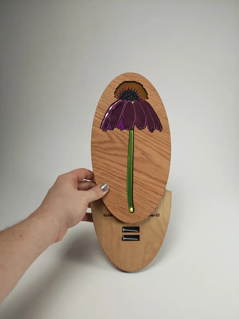 Coneflower 1 held up beside its oval oak mounting backer, which shows two black standoffs and an engraved kevcreates.art label